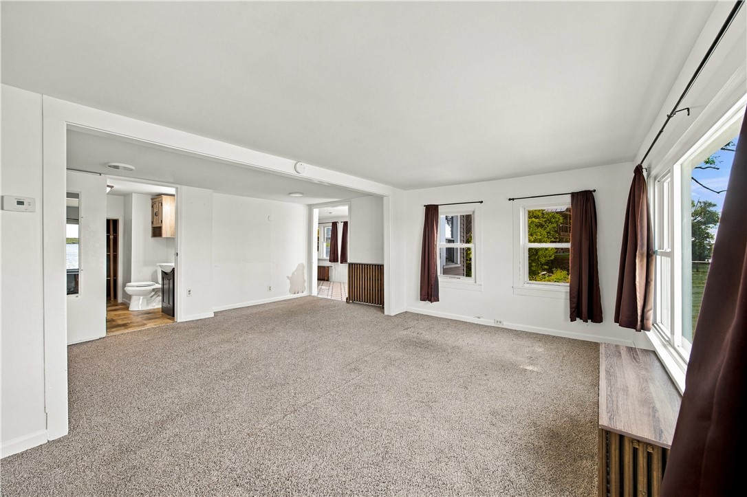 Mostly vacant carpeted living room with dark curtains, a sliding glass door, and water visible through a window.