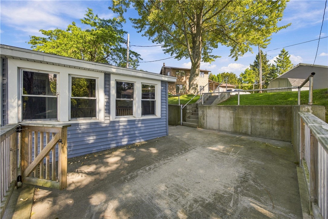 Concrete patio beside a blue-sided house, with a retaining wall and steps to the yard.