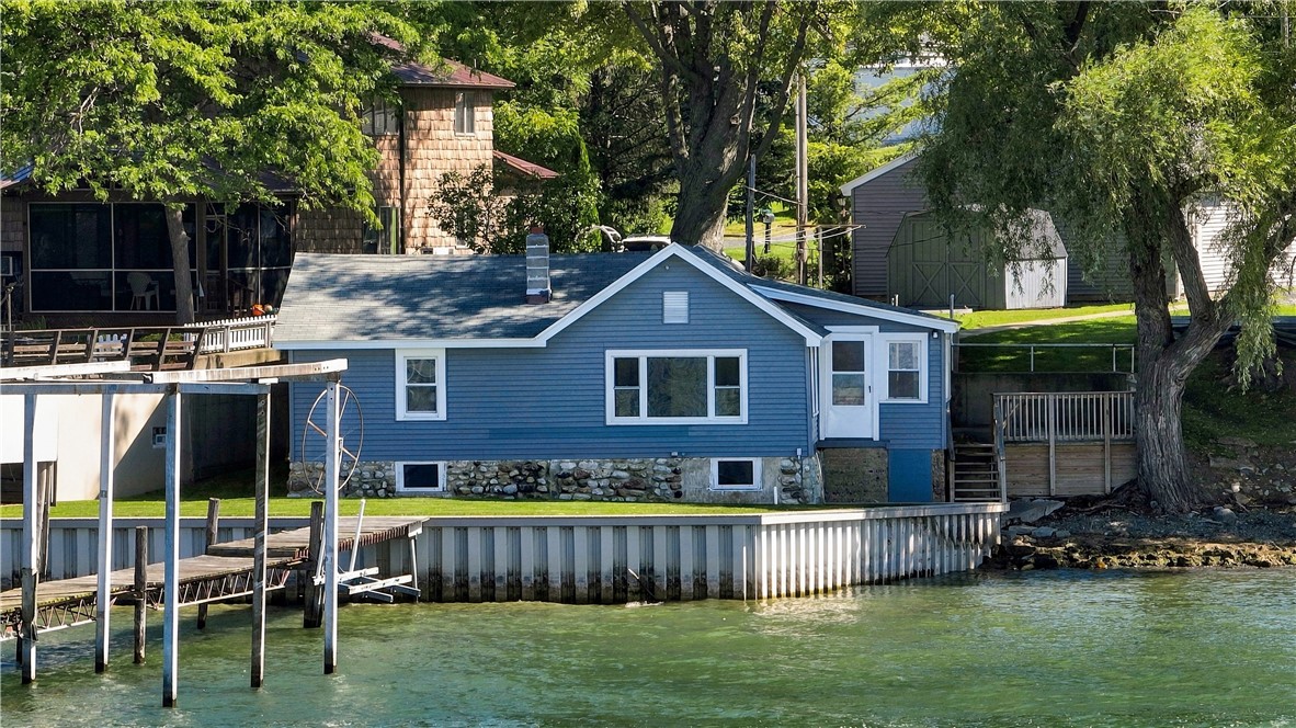 Blue lakeside house with a dock extending over the water and mature trees along the shore.