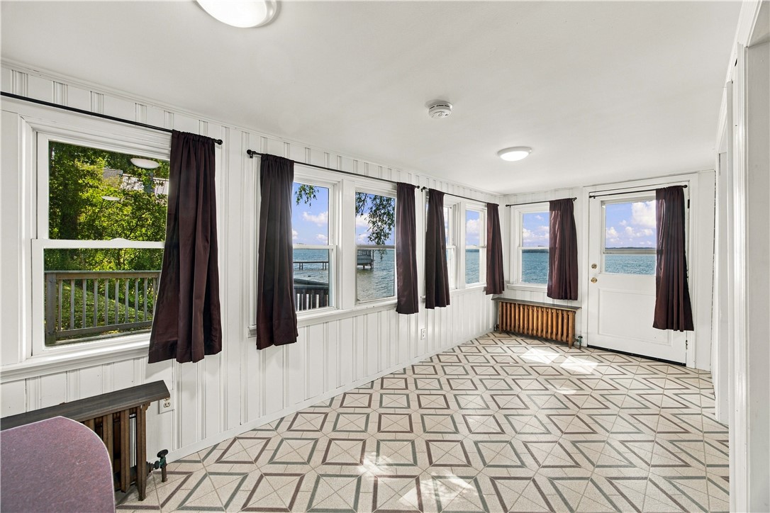 Vacant sunroom with geometric tile flooring and windows overlooking the lake.
