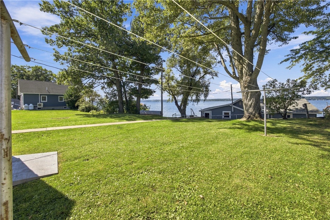 Lakeside lawn with mature trees, a clothesline, and small buildings beside the water.