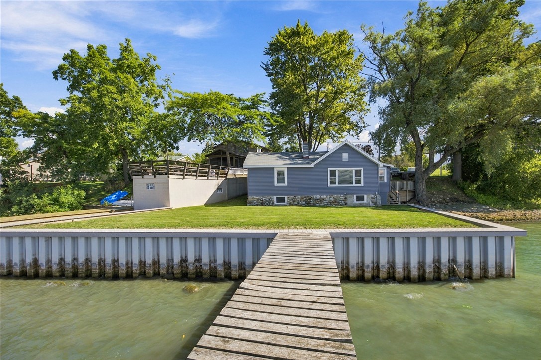 Gray lakeside house behind a grassy yard, with a wooden dock extending over the water.
