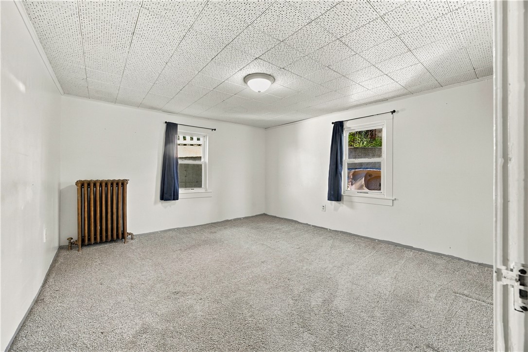 Vacant carpeted room with two curtained windows and a cast-iron radiator.