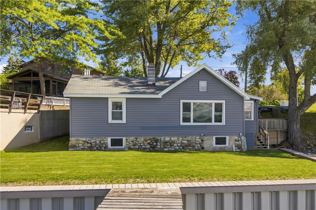 Gray house with a stone foundation and broad lawn beside a wooden dock.