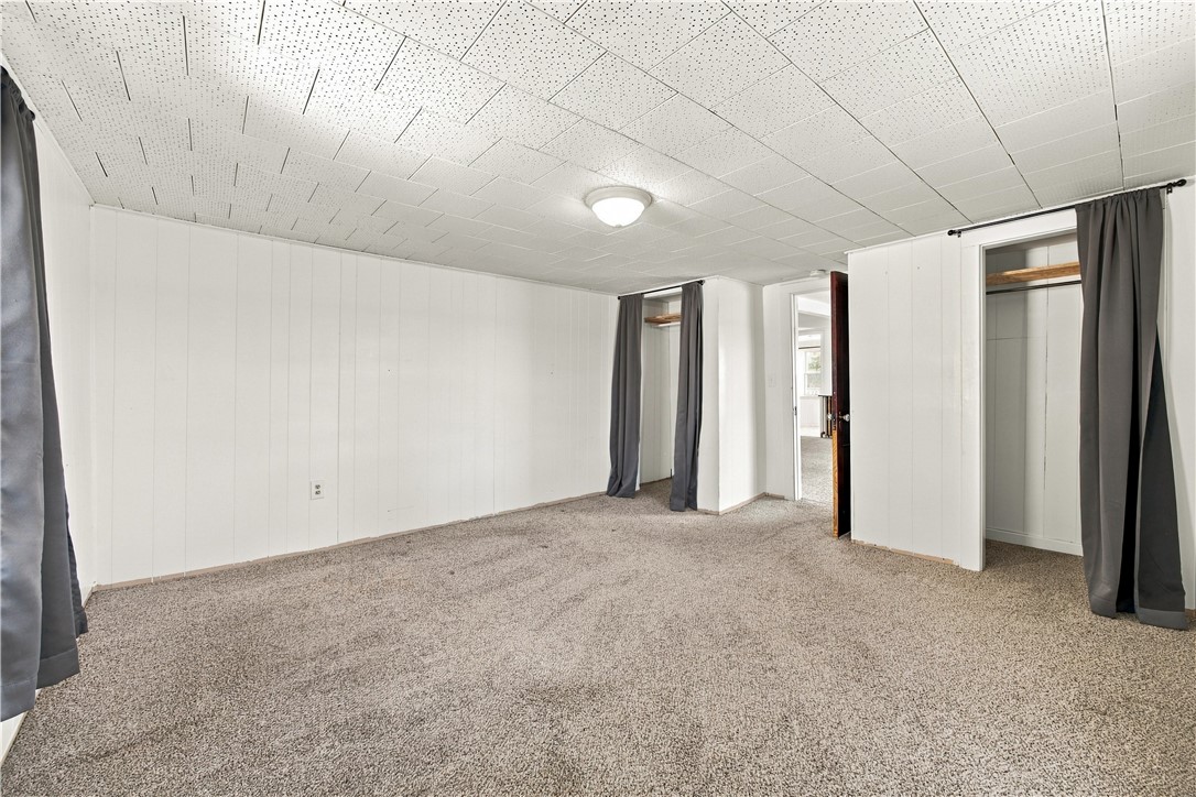 Empty carpeted room with white paneled walls and curtained closet openings.