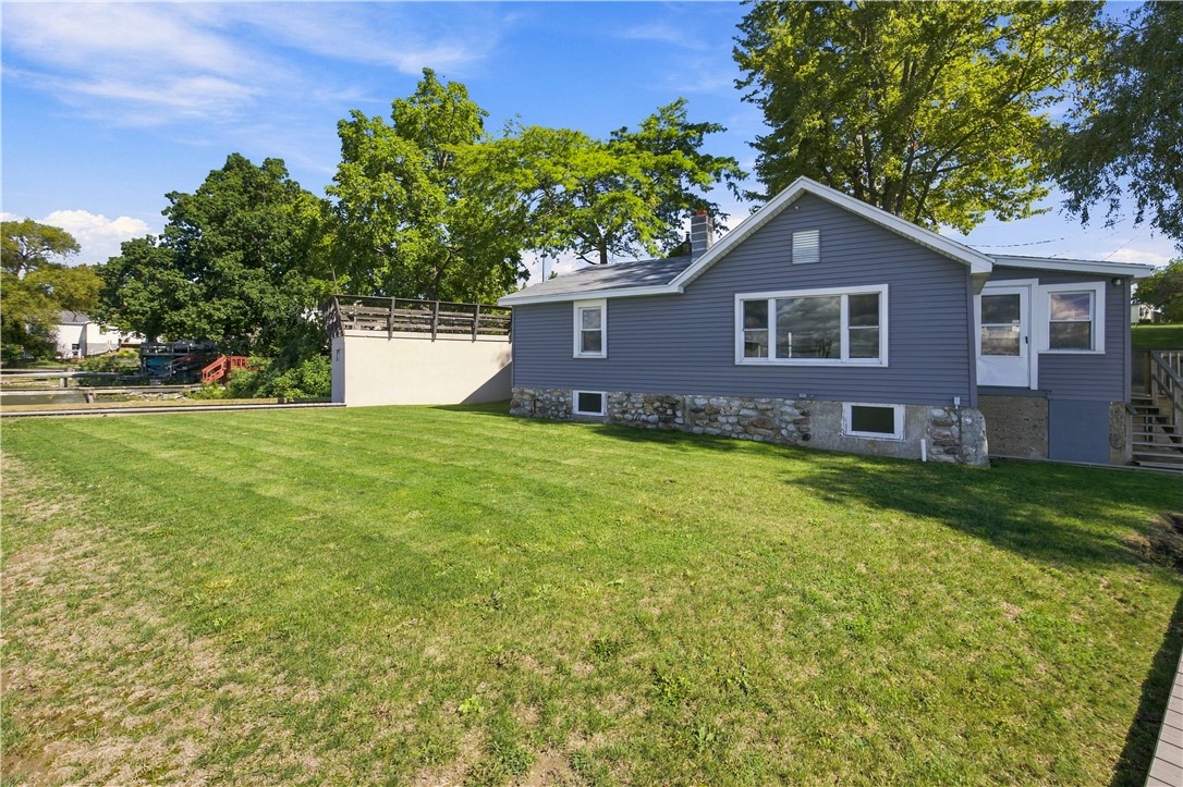 Rear exterior of a gray house with a stone foundation, raised deck, and broad lawn.