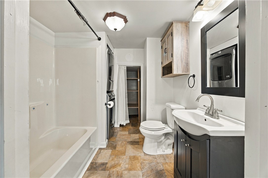 Bathroom with a bathtub, stacked washer and dryer, and dark vanity with a white sink.