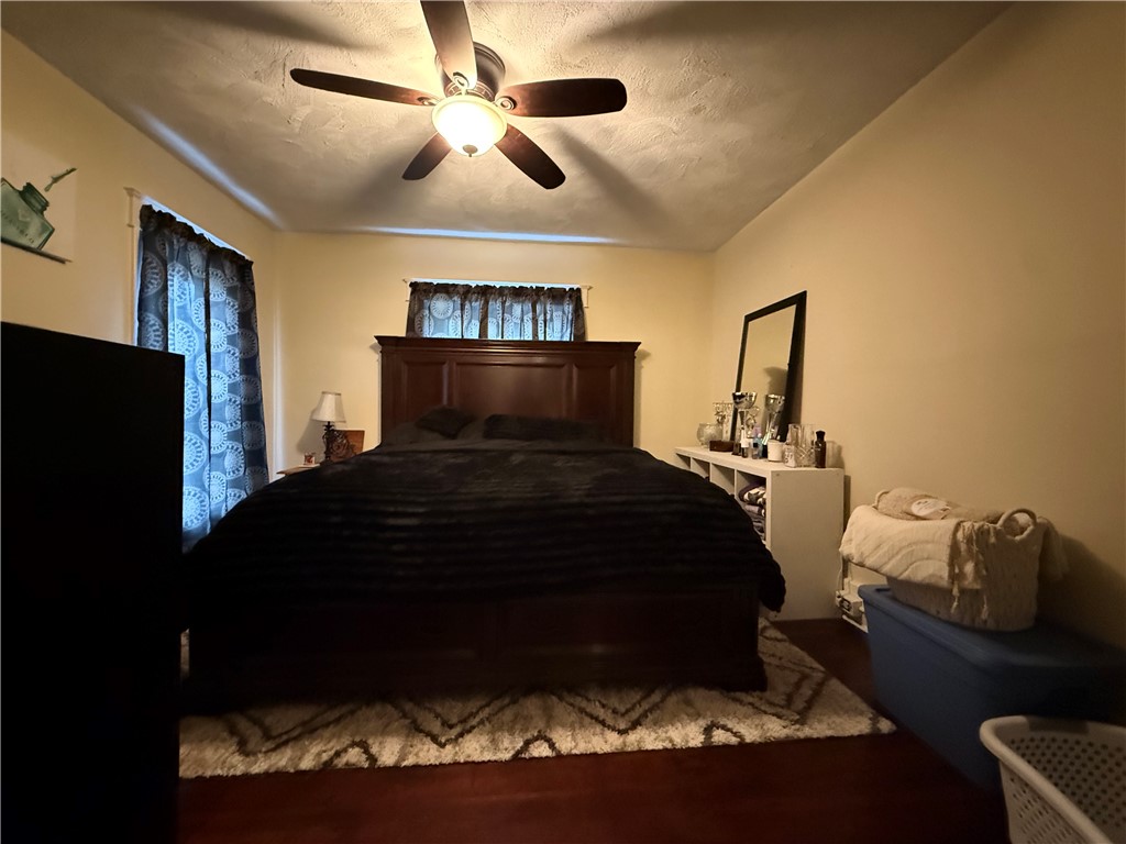Furnished bedroom with a dark wood bed, ceiling fan, blue patterned curtains, and geometric rug.
