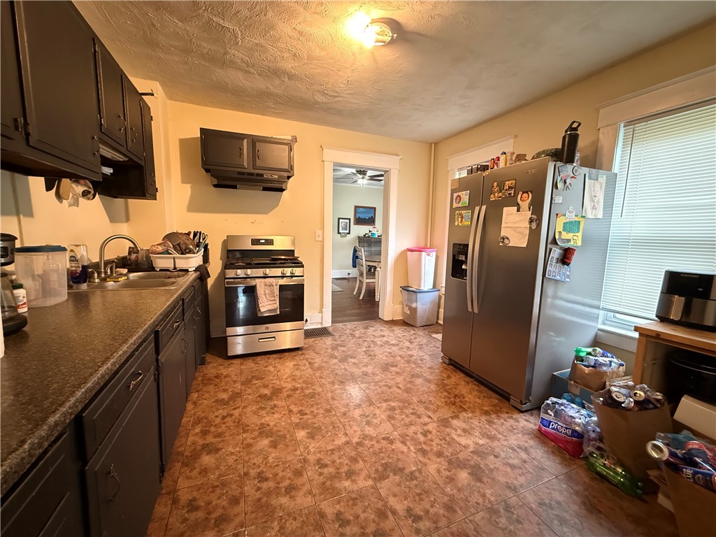 Kitchen with dark cabinets, stainless steel appliances, patterned tile flooring, and a doorway to the dining area.