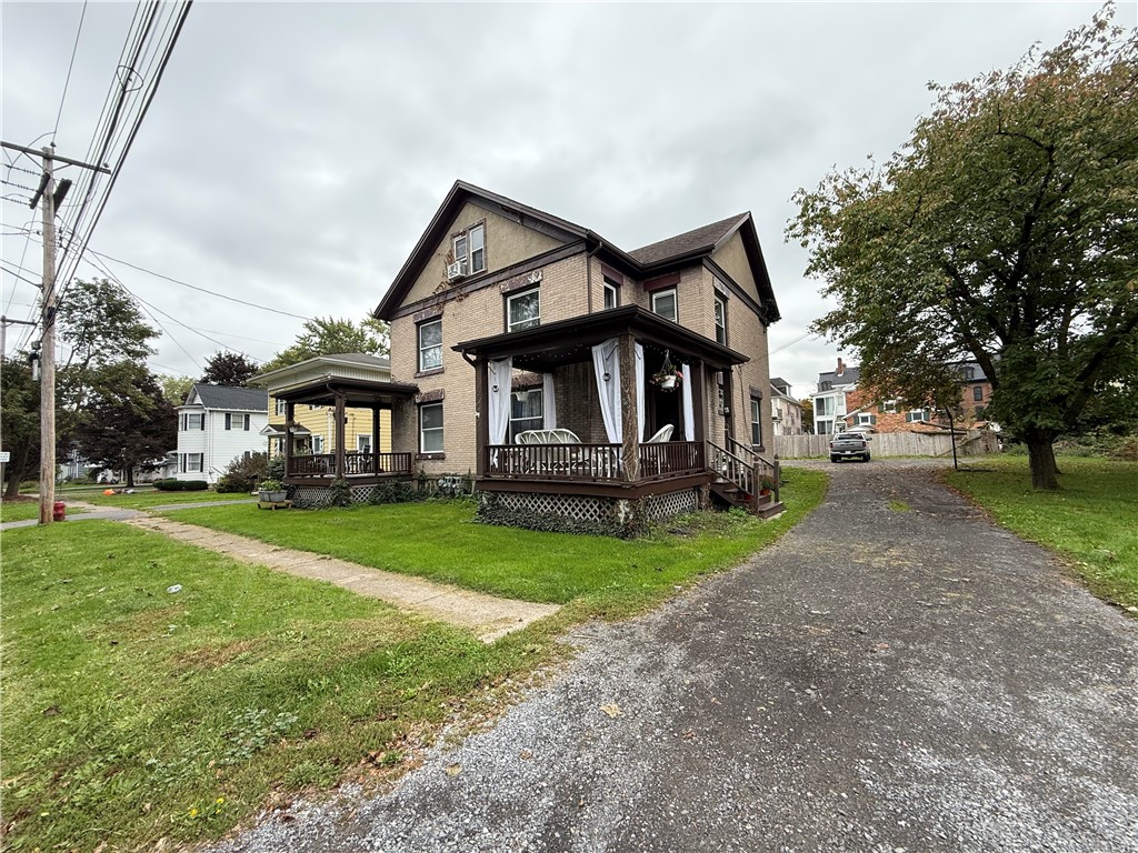 Two-story tan brick house with a covered porch beside a gravel driveway.