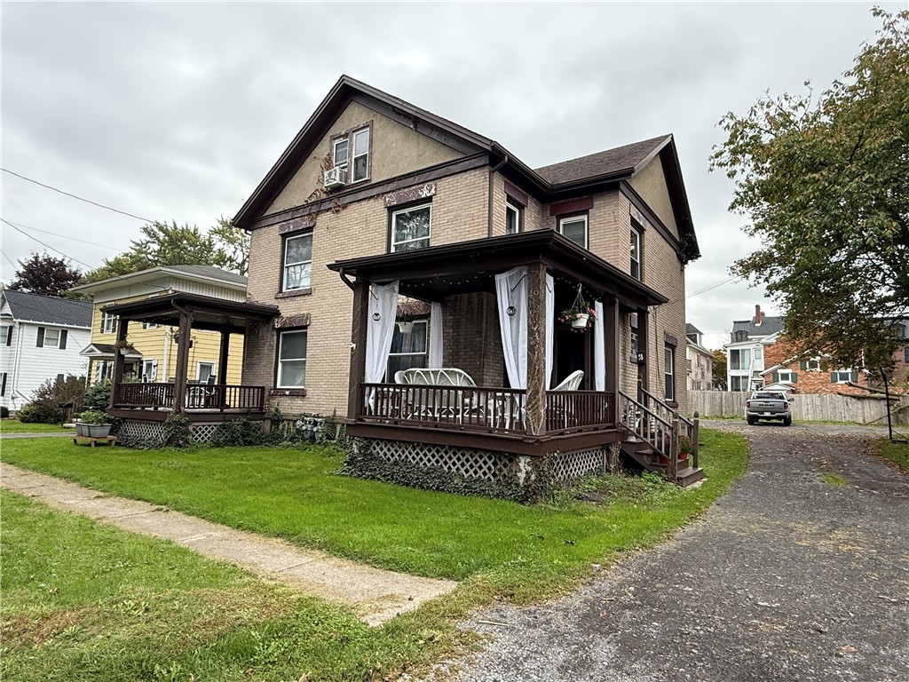 Two-story brick house with a covered wooden porch, white curtains, and a front lawn.