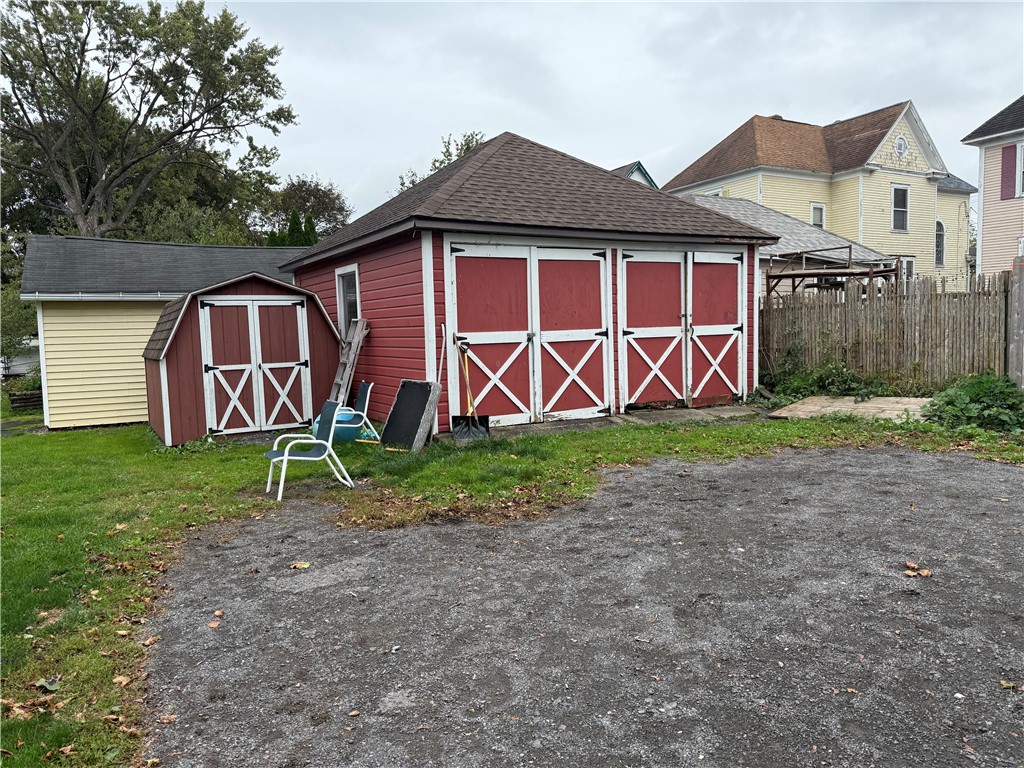 Red detached garage with white-trimmed barn doors beside a smaller matching shed.
