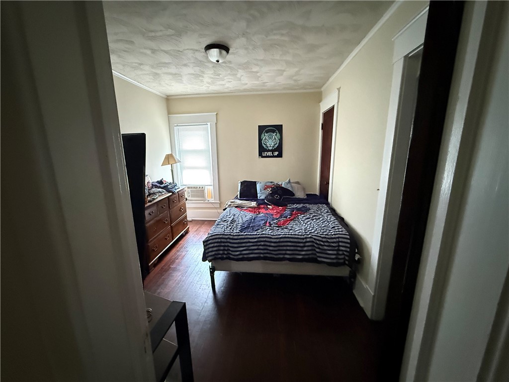 Bedroom with a striped bedspread, wooden dresser, and window air conditioner.