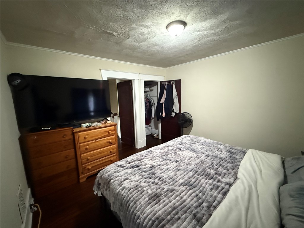 Bedroom with a gray quilted bed, wooden dressers, and an open closet.