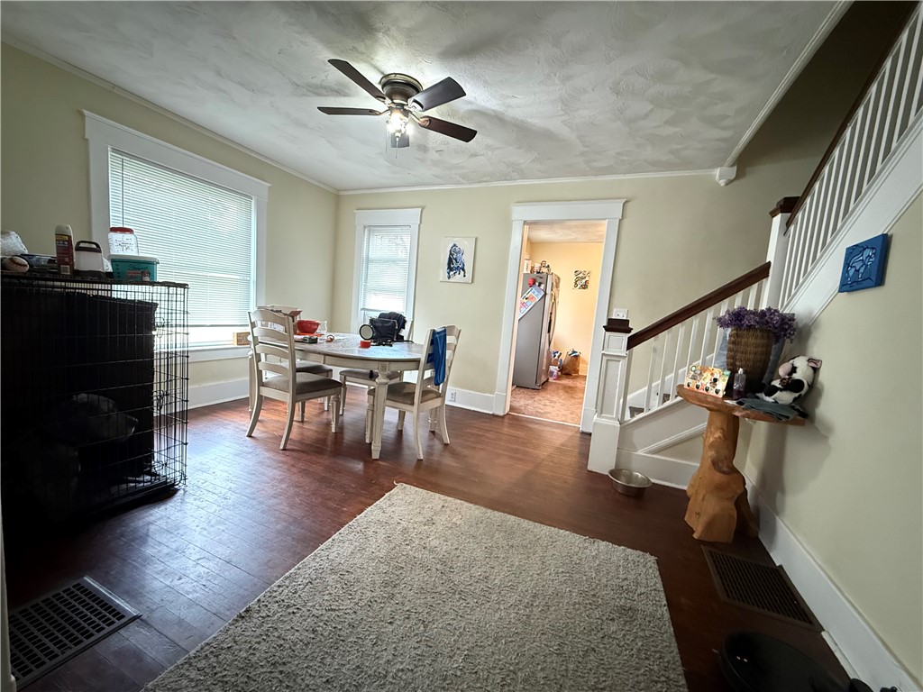 Dining area with a round table beside large windows and a staircase with white balusters.