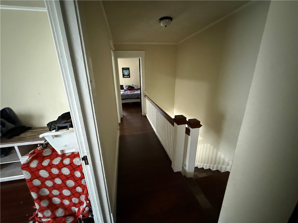 Upstairs hallway with dark wood floors, a white stair railing, and a bedroom at the end.