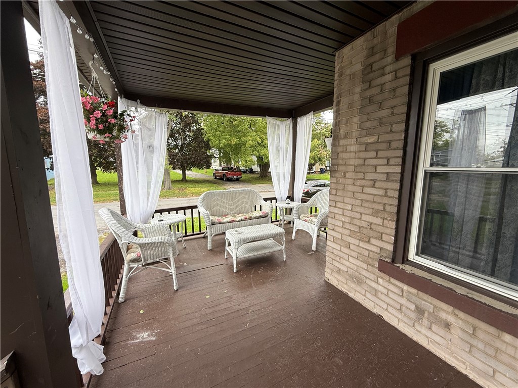 Covered porch with white wicker seating, sheer curtains, and a view of the leafy yard.