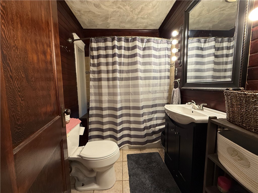 Bathroom with dark wood paneling, a striped shower curtain, and a large framed mirror.