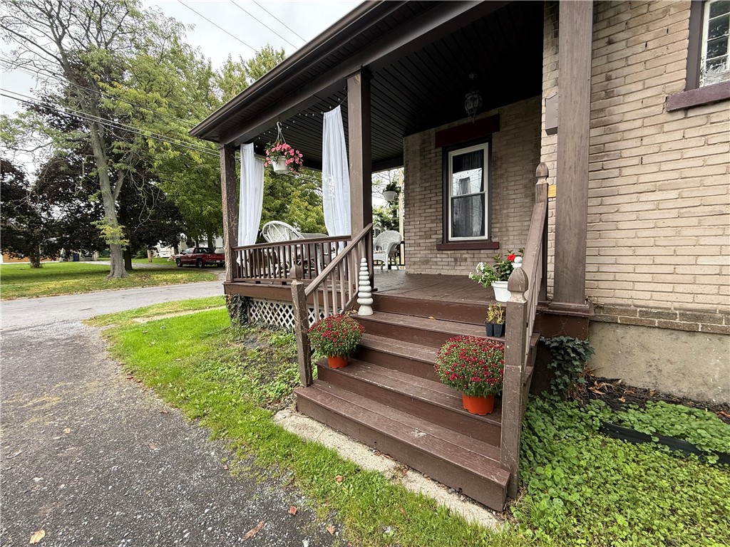 Brick house with a covered porch, brown wooden steps, white curtains, and potted flowers.