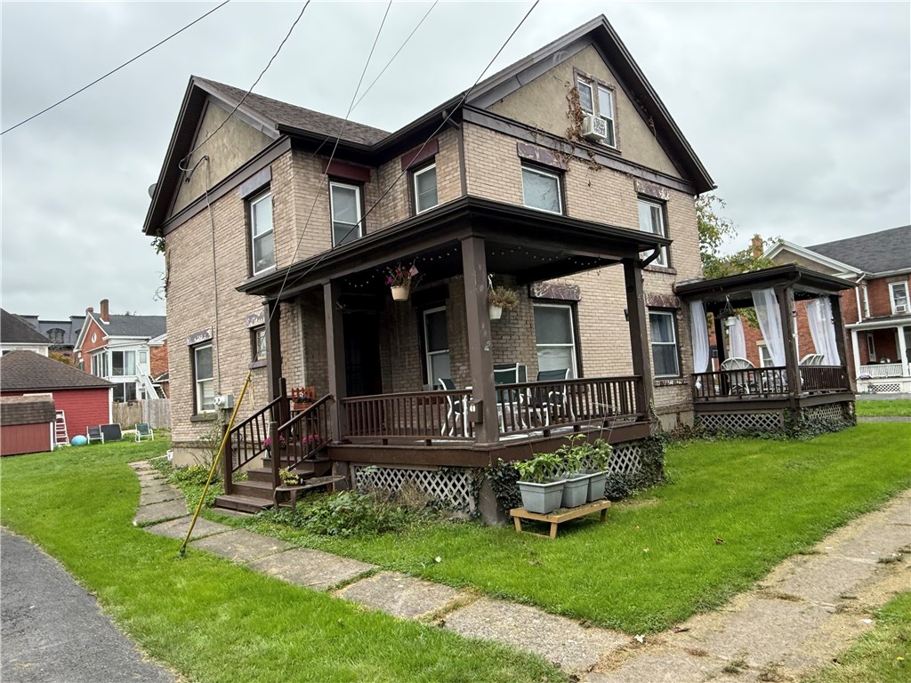 Two-story brick house with a large covered porch and green lawn.