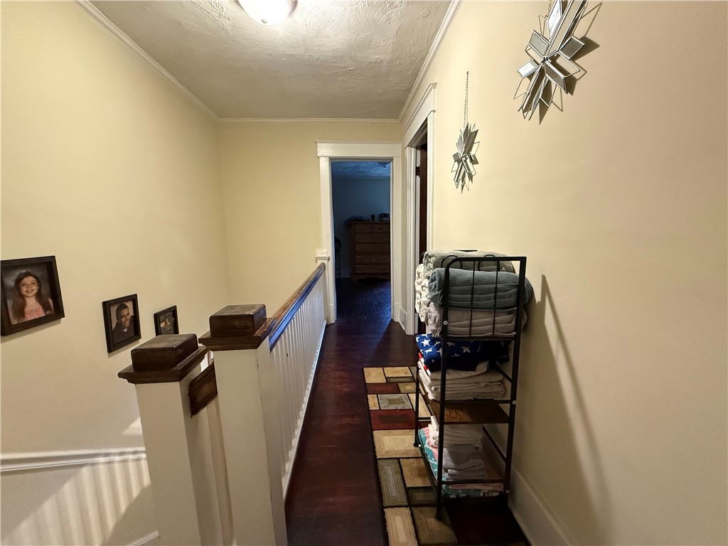 Upstairs hallway with dark hardwood floors, white stair railing, framed portraits, and a rack of folded linens.