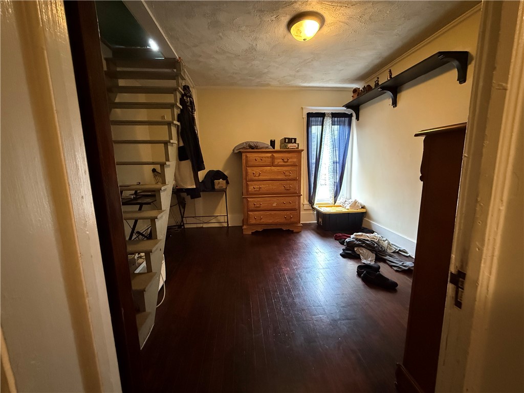 Bedroom with a steep open staircase, wooden dresser, and dark wood flooring.