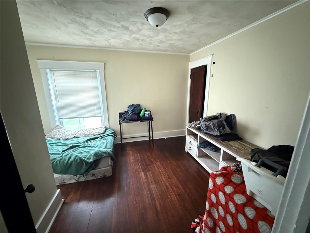 Bedroom with teal bedding, a window with blinds, dark wood floors, and a long white storage unit.