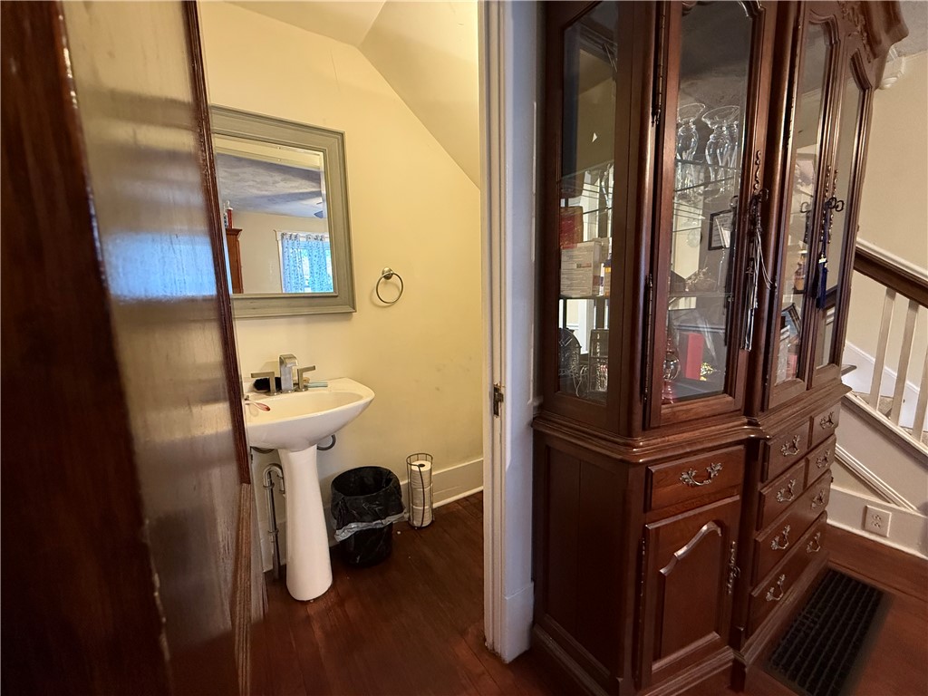 Small bathroom with a white pedestal sink beside a dark-wood glass-front display cabinet.