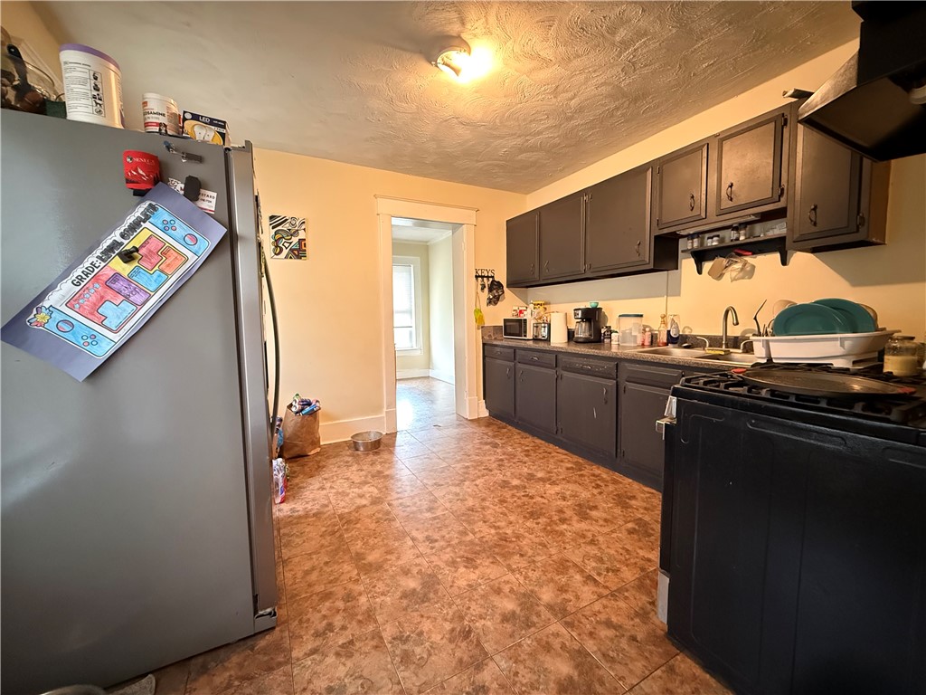 Kitchen with dark cabinets, a stainless steel refrigerator, gas range, and patterned tile floor.
