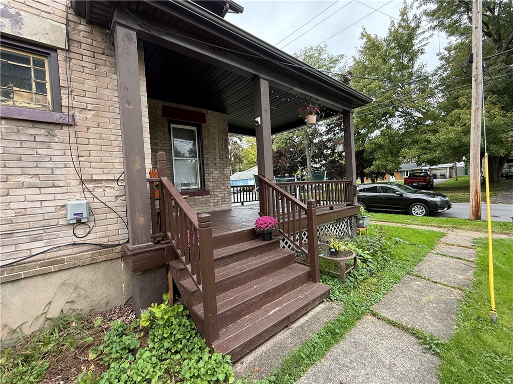Brick home with a covered porch, brown wooden steps, flower planters, and a walkway to the sidewalk.