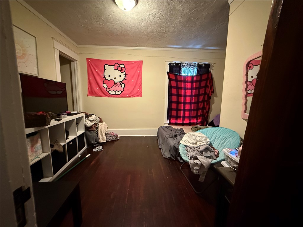 Bedroom with dark hardwood floors, a pink Hello Kitty wall hanging, and a red plaid window covering.