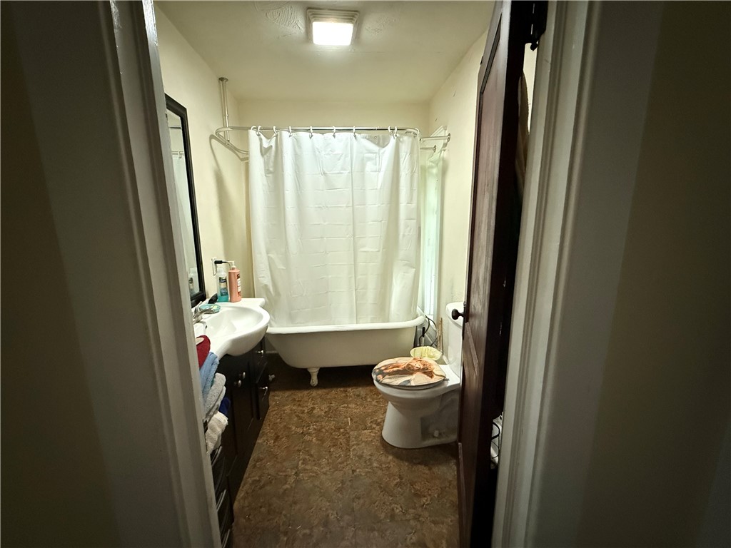 Bathroom with a white tub and shower curtain, sink with dark vanity, and toilet.