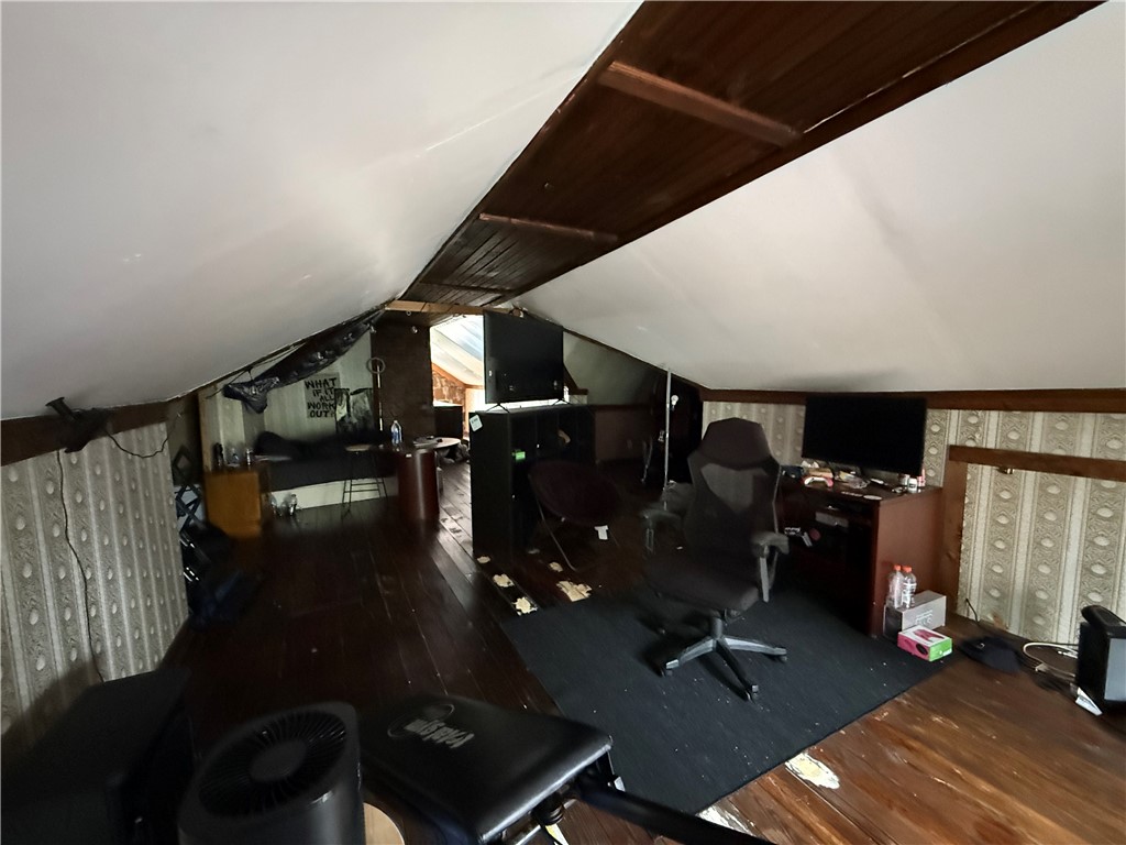 Attic workspace with sloped ceilings, a dark wood beam, office chairs, desks, and wood flooring.