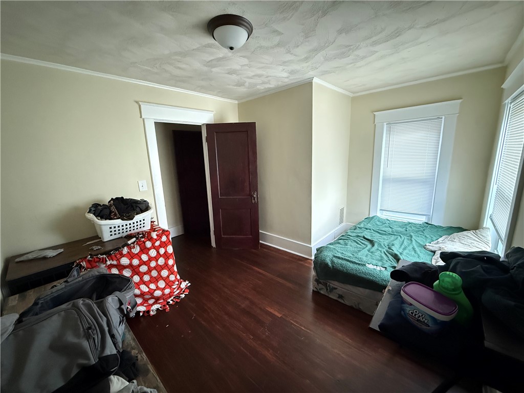Bedroom with a bed by two windows, dark hardwood floors, and a textured ceiling.