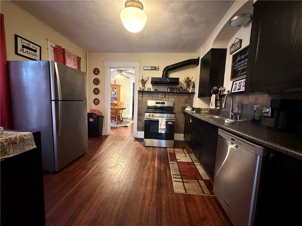 Kitchen with dark cabinets, stainless steel appliances, tile backsplash, and wood floors.