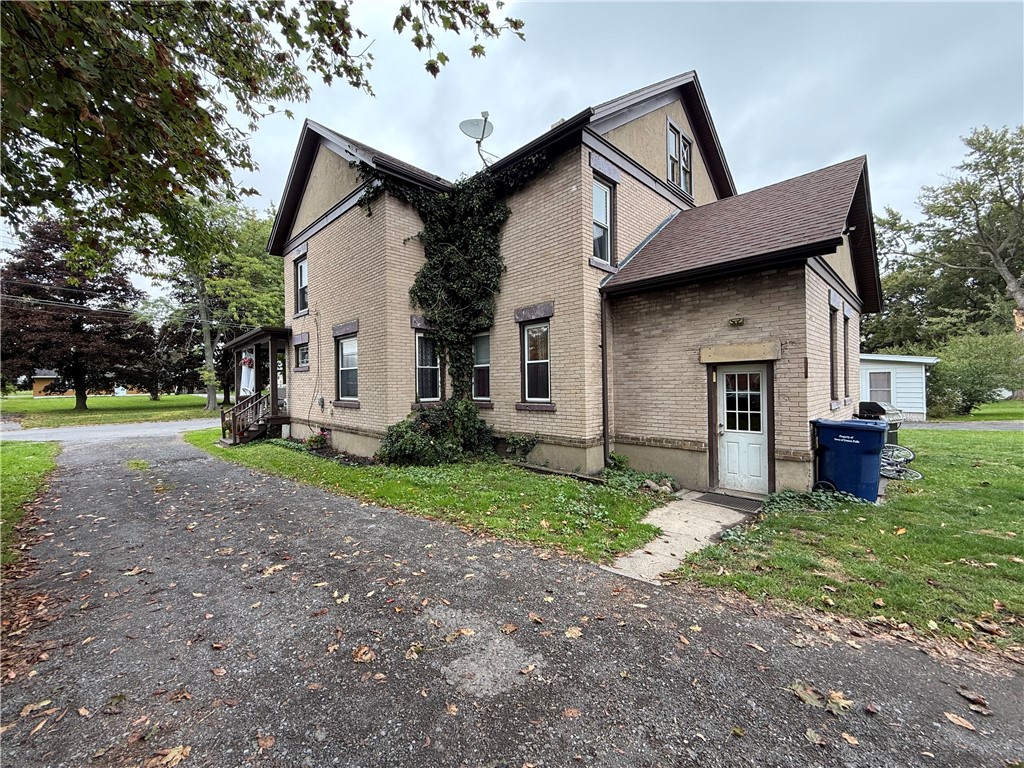 Two-story tan brick house with ivy climbing the facade and a paved driveway.