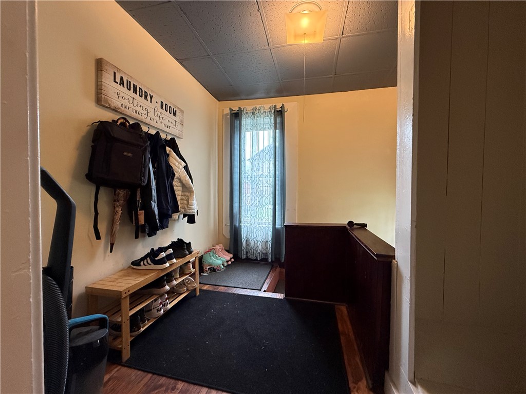 Entryway with a coat rack, shoe bench, patterned window curtain, and laundry room sign.