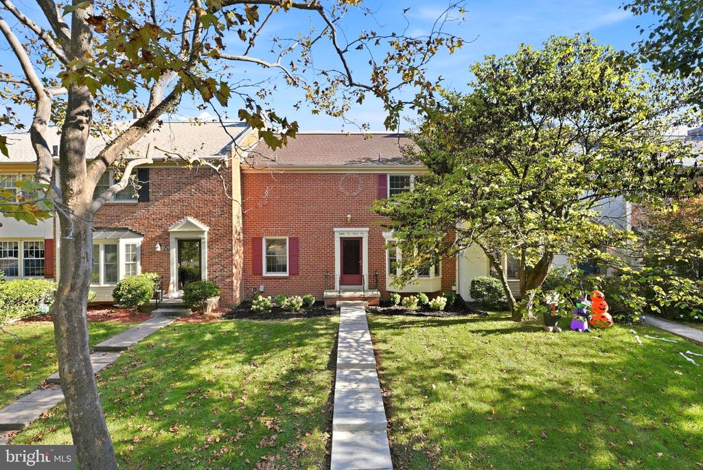 Brick row house with a red front door, a straight walkway, and mature trees.