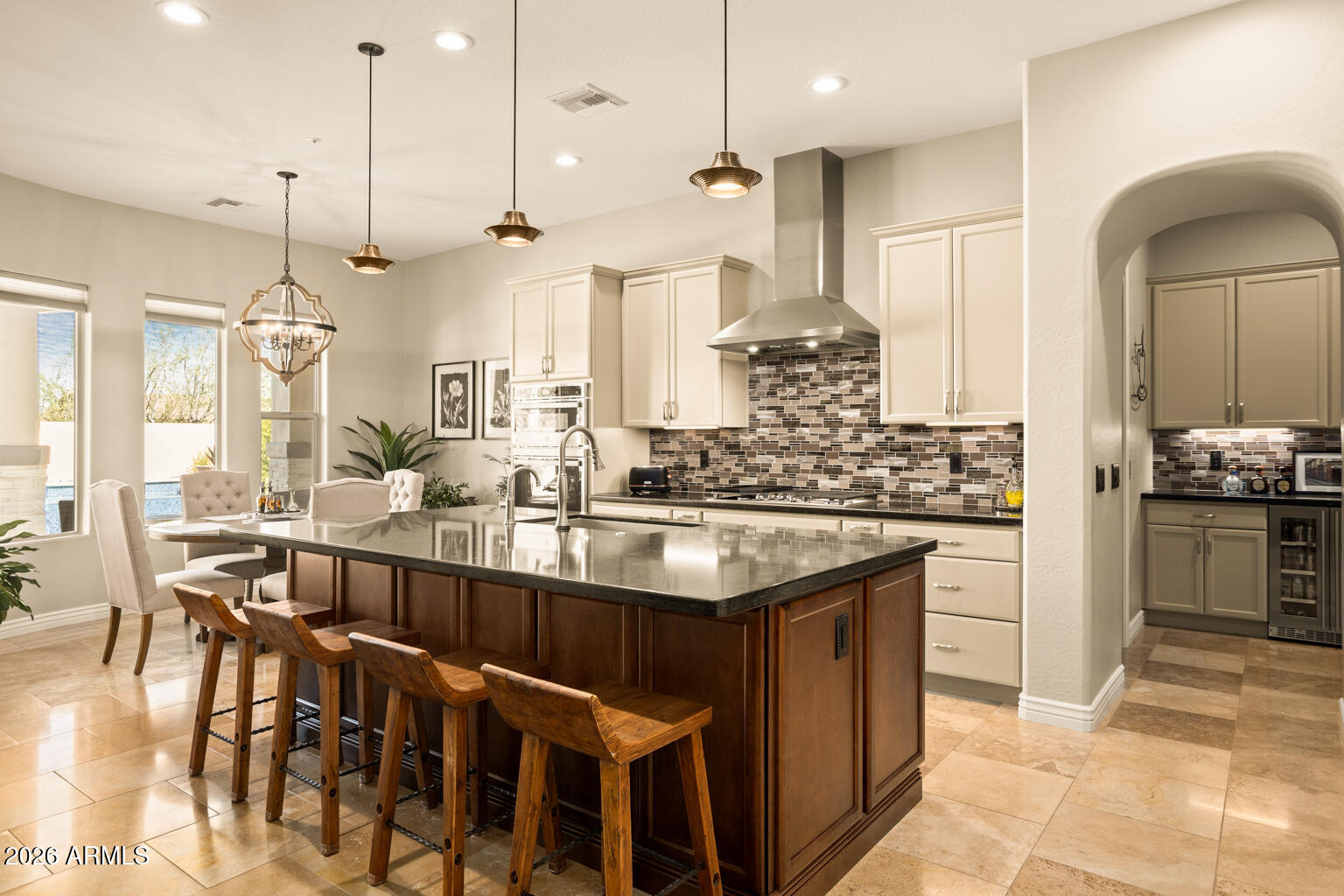 Kitchen with a large wood island, bar stools, cream cabinetry, and mosaic tile backsplash.