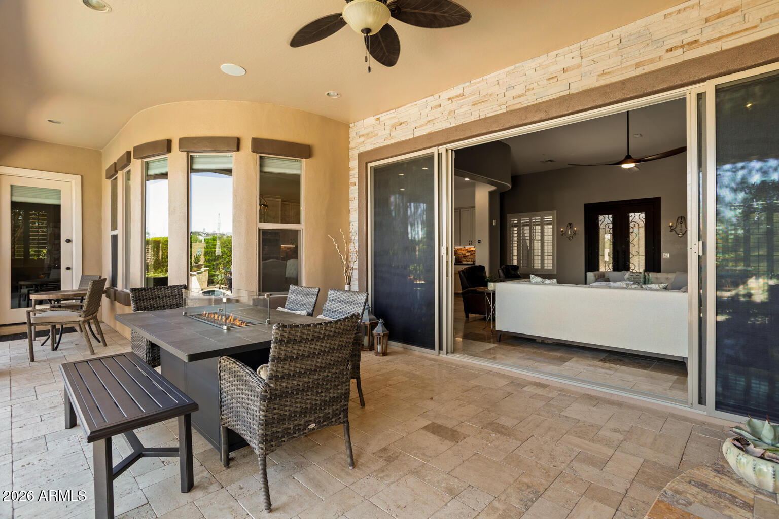 Covered patio with a fire-feature dining table, wicker chairs, and wide sliding doors to the living room.