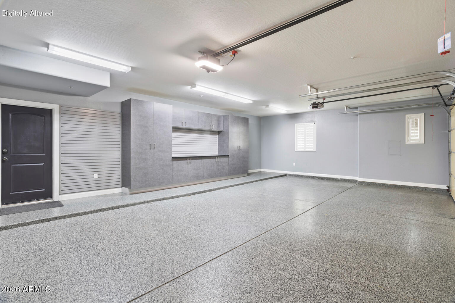 Empty garage with a speckled epoxy floor and built-in gray storage cabinets.