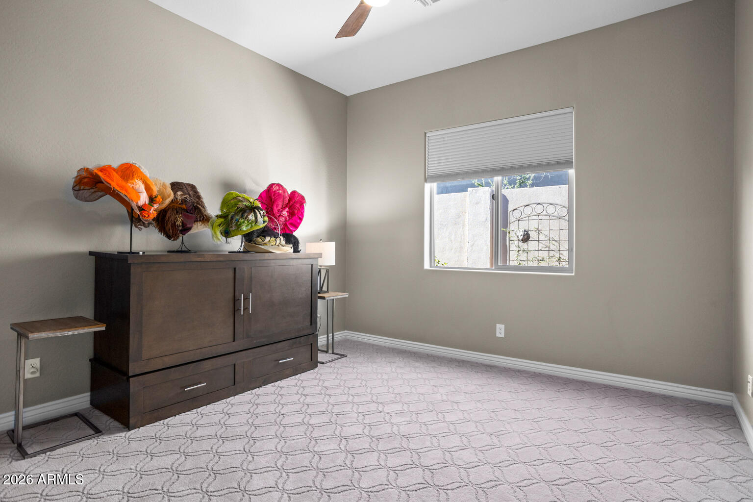 Bedroom with patterned carpet, window, and dark cabinet displaying colorful hats.