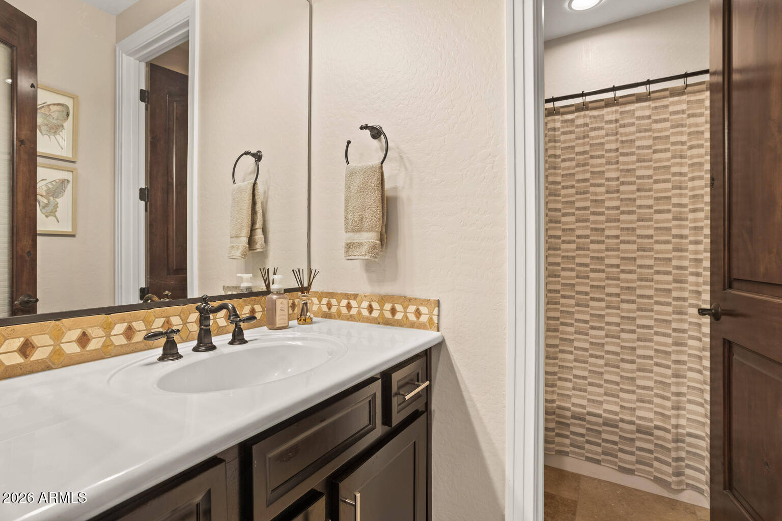 Bathroom vanity with geometric tile backsplash and striped shower curtain.