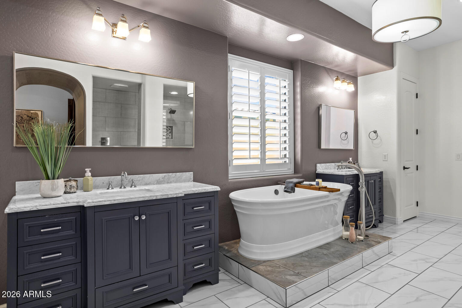 Bathroom with a freestanding soaking tub, dark vanities, marble countertops, and shuttered windows.