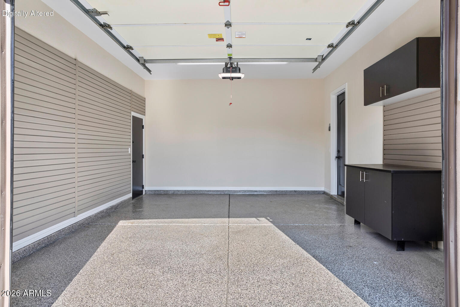 Vacant garage with gray slatwall panels, dark built-in cabinets and a speckled concrete floor.
