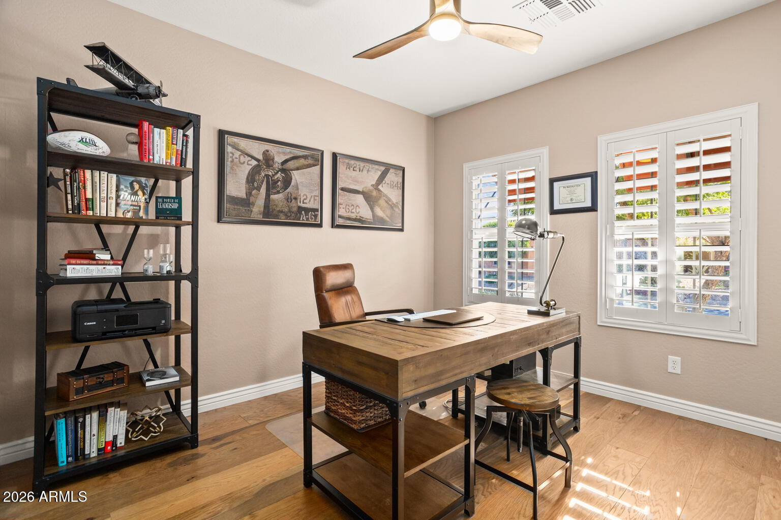 Home office with a large wooden desk, leather chair, aviation prints, and plantation shutters.