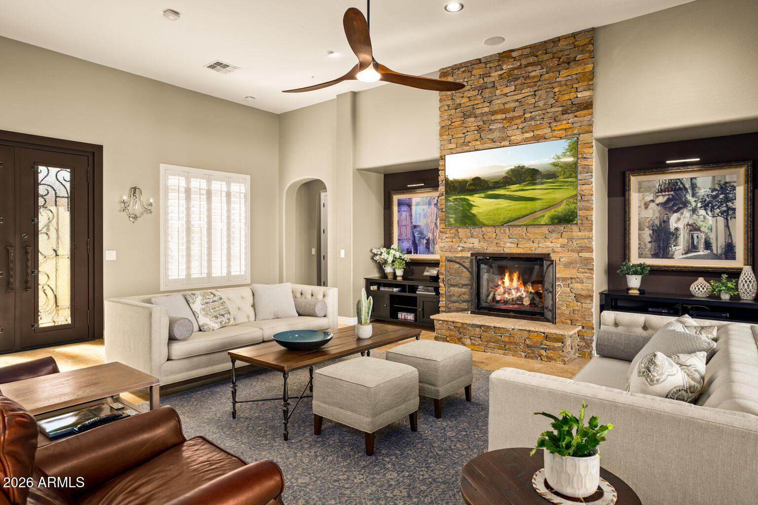 Living room with a tall stone fireplace, lit fire, high ceiling, and light sofas.