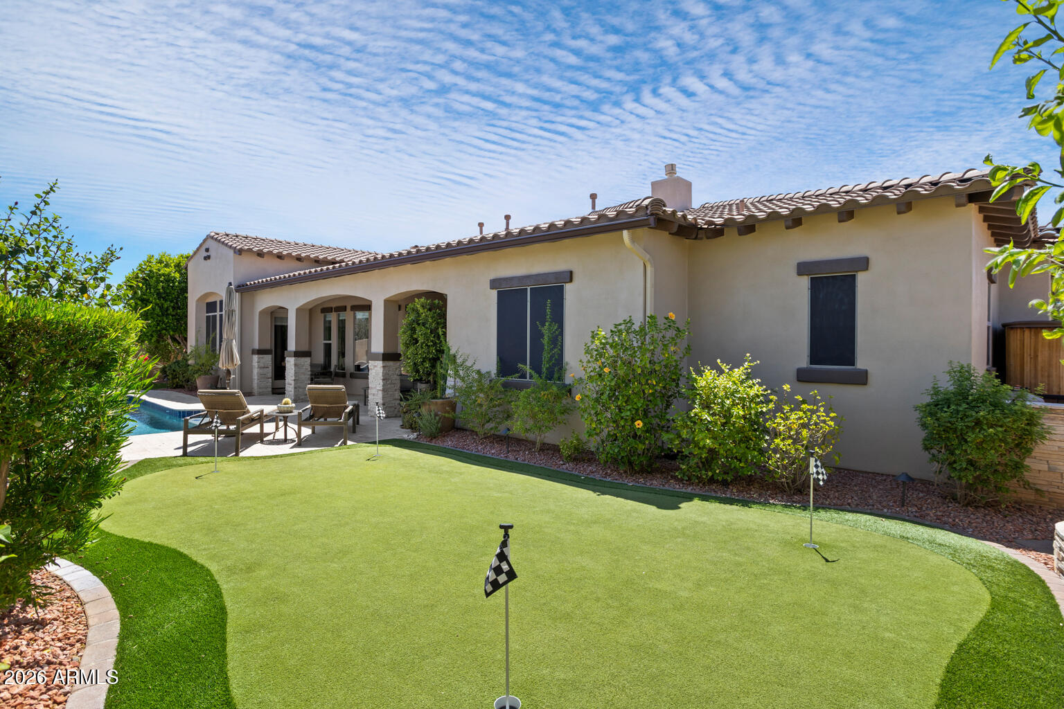 Home’s rear patio and pool overlook a backyard putting green with golf flags.