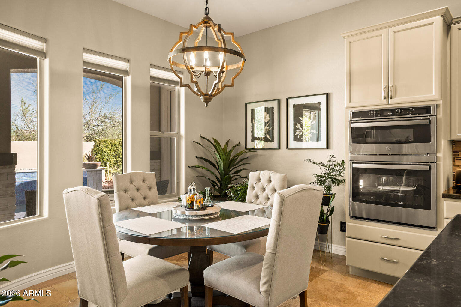 Dining area with a glass-top table, upholstered chairs, chandelier, and built-in double ovens.
