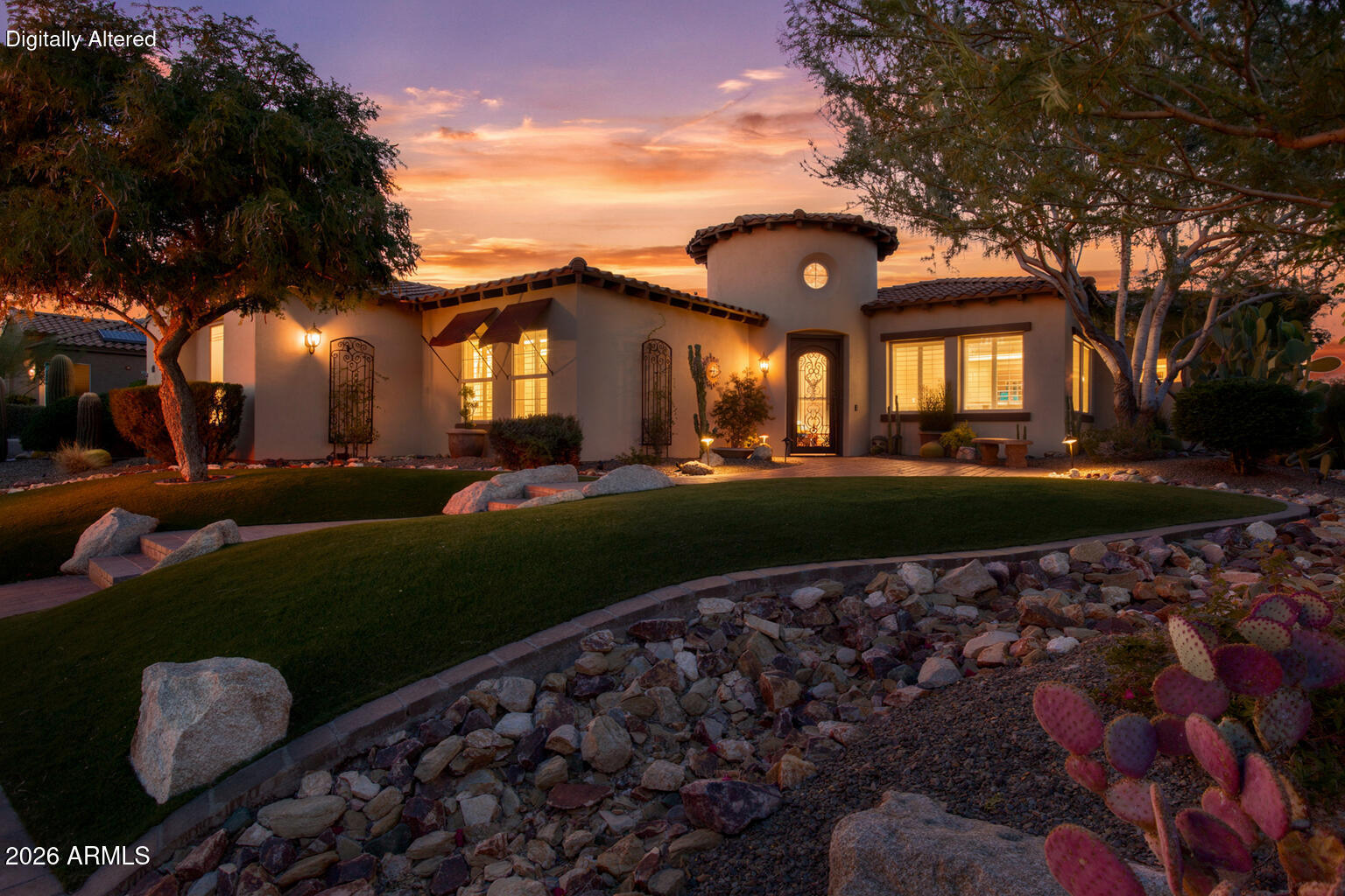 Stucco home with a tiled roof, circular tower window, and desert landscaping at dusk.